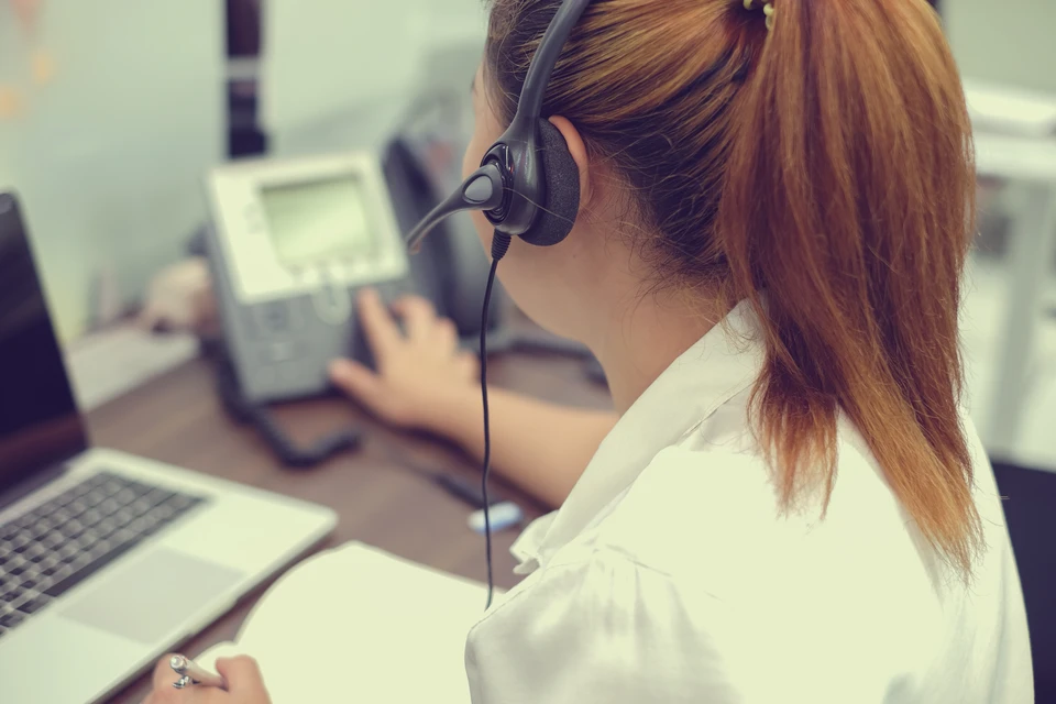 Femme en chemise blanche travaillant dans un centre d'appels, portant un casque téléphonique professionnel avec micro-perche