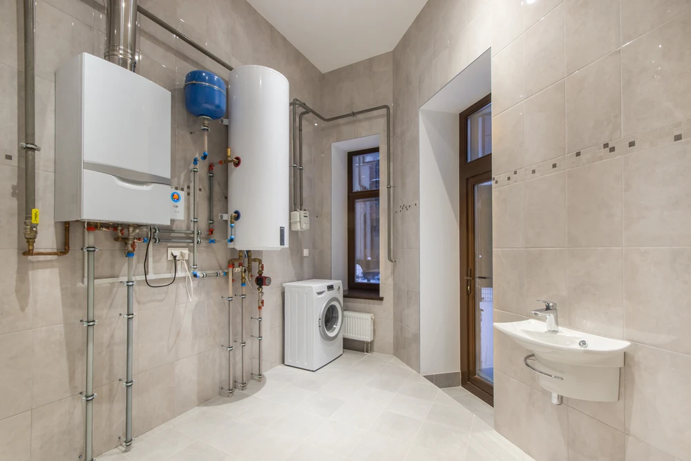 Salle technique moderne avec chaudière murale blanche, ballon d'eau chaude vertical, système de plomberie apparent avec vannes et raccords colorés