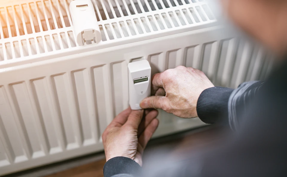 Personne âgée ajustant un thermostat de radiateur à eau chaude dans un intérieur domestique