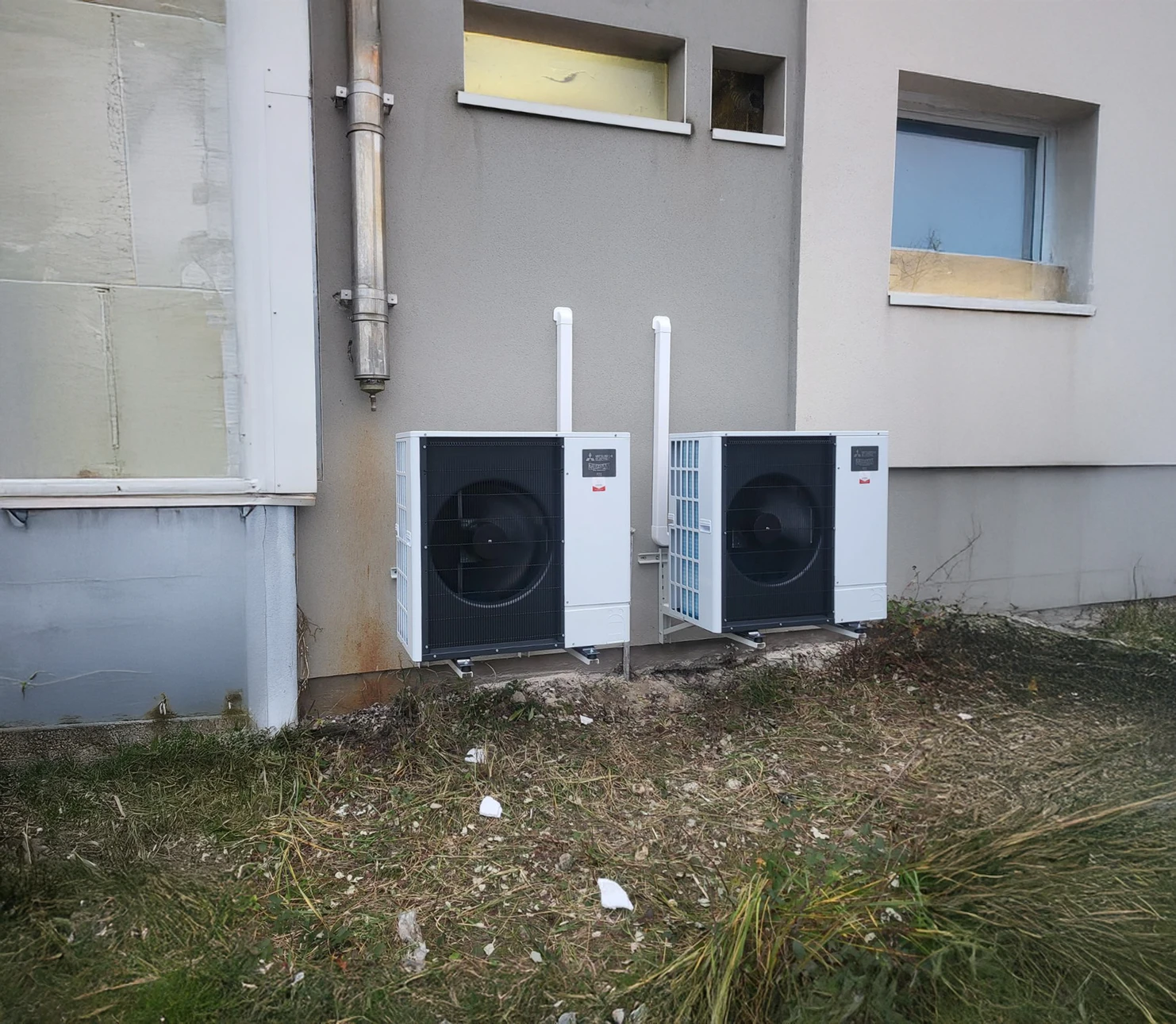 Placé près du mur d'un cottage moderne, l'unité extérieure d'une pompe à chaleur est visible